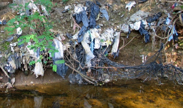 I rifiuti dell’ex discarica emergono nel torrente Bozzente (foto Blitz)