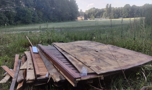 Assi e tavole di legno abbandonate, insieme ai sacchi di rifiuti, nel verde dietro alla ciclabile, a Capolago